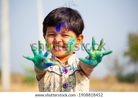young cute cheerful little girl kid with applied holi colors powder showing colorful hands to camera during holi festival celebration