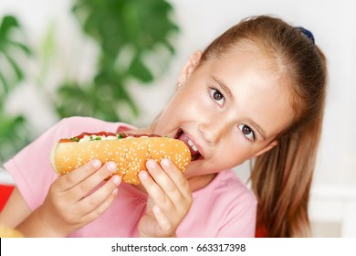 Young Cute European Girl In T-shirt Is Eating Unhealthy Food Like Hot Dog And Chips At Sunny Day