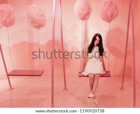 Young cute girl with black hair is riding on a swing on a bright pink background in the form of clouds