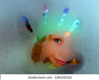 A Young Cute Girl And Her Beautiful Eyes Behind A Frosty Car Glass Window During A Winter Time. Unique, Special  And Inventive Child, Creativity In The Childhood, Green Eyes, Hello And Bye Hand,finger