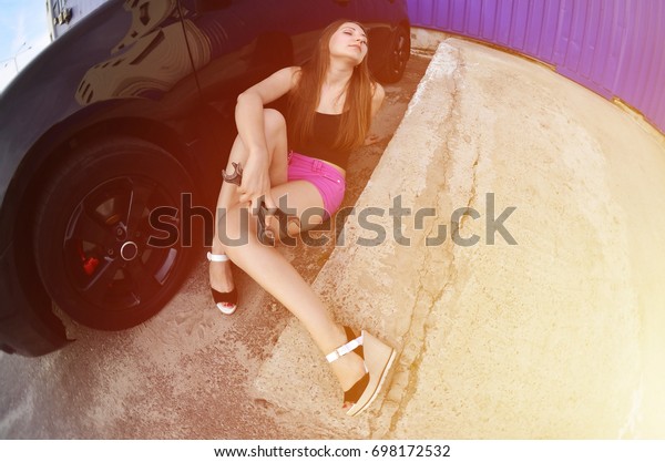 Young cute girl\
in pink shorts and black shirt with wrenches near a black car with\
an open hood. The concept of repair and maintenance of a car in the\
performance of a\
girl-mechanic