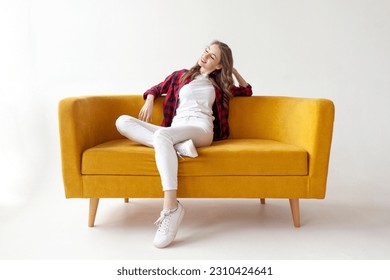 young cute girl sits on soft comfortable sofa and relaxes, pensive woman is resting on yellow couch on white isolated background - Powered by Shutterstock