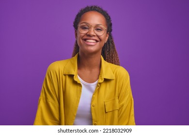 Young cute happy African American woman zoomer in casual clothes laughing and looking at camera radiating optimism and positive emotions stands on plain purple background. Good mood concept