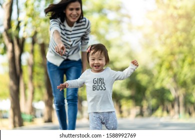 Young Cute Happy Little Asian Toddler Girl Running In Park With Mother. Mom Taking Care Daughter By Following And Hold Child Carefully. Kid Smiling Enjoy Learning To Walk And Run, Family Relation.