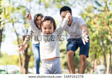 Young cute happy little Asian toddler girl running in park with parents. Mom dad taking care daughter by following looking after carefully. Kid smiling enjoy learning to walk and run, family relation.