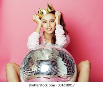 young cute party girl on pink background with  ball and crown smiling