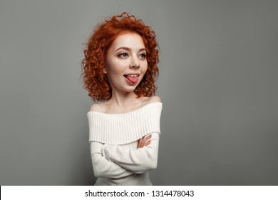 young cute redhead curly haired girl shows her tongue teasing on the gray backgroun in studio