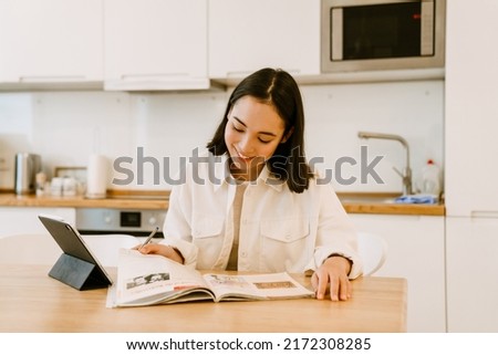 Young cute smiling asian woman with tablet studying at home