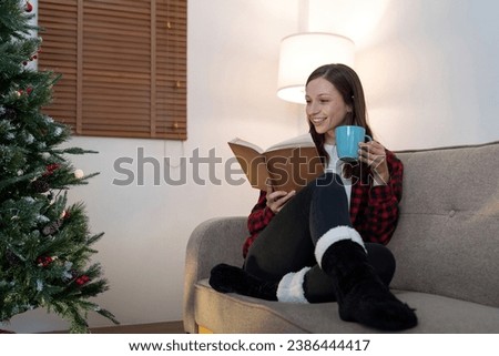 Young cute woman holding cup coffee or tea and read interest book. Concept of Christmas atmosphere at home