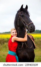 Young cute woman in saturate long dress with black strong and muscular horse in field