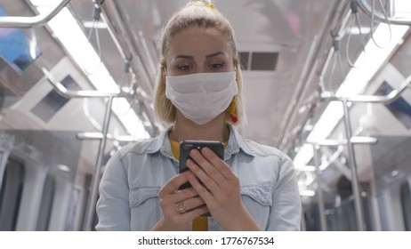 Young cute woman sitting on the subway, listening to music, holding phones, a smartphone, answering texts, letters, messages.Woman wearing a protective mask. - Shutterstock ID 1776767534