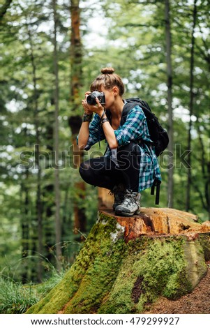 young cute woman traveling alone with backpack and camera, in the middle of a forest, taking pictures of wildlife