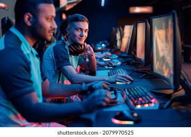 Young cybersport gamer looking at camera and smiling while sitting in front of PC monitor in cyber club