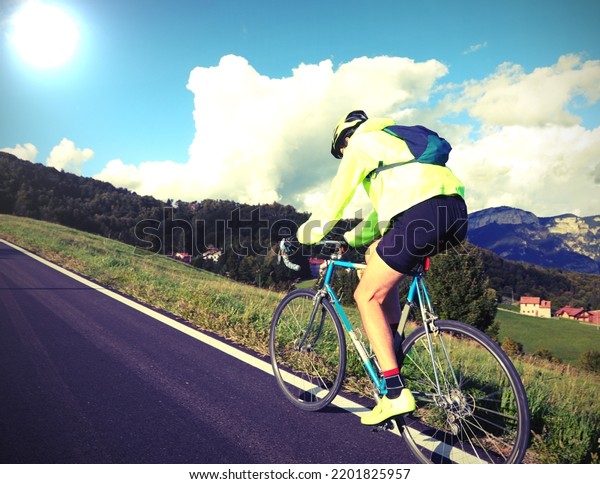 young cyclist with racing bicycle and\
phosphorescent waterproof jacket on a mountain\
road