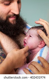 A Young Dad Holds His Newborn Son With Family Members Hands Coming In To Investigate The Baby.  The Dad Has A Full Beard And Is Shirtless For Skin On Skin, Bonding Contact With His Infant.