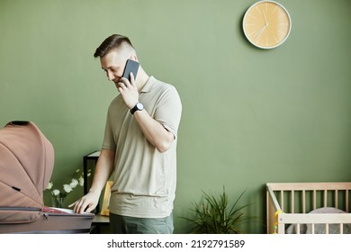 Young Dad Talking On Mobile Phone While Babysitting With His Baby In Pram In The Room