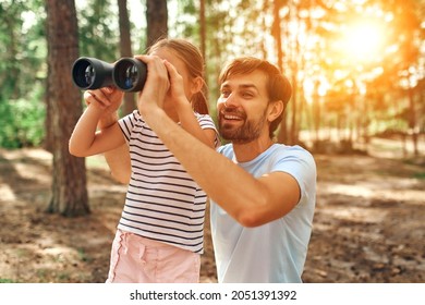 Young dad teaches his little daughter to look through binoculars in a pine forest. Camping, recreation, hiking. - Powered by Shutterstock