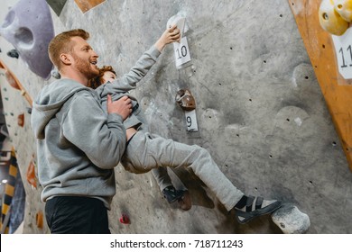 Young dad teaching his little son how to climb a wall with grips at gym - Powered by Shutterstock