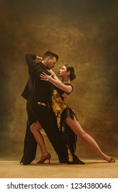 The Young Dance Ballroom Couple In Gold Dress Dancing In Sensual Pose On Studio Background. Professional Dancers Dancing Tango. Ballroom Dance Concept. Human Emotions - Love And Passion