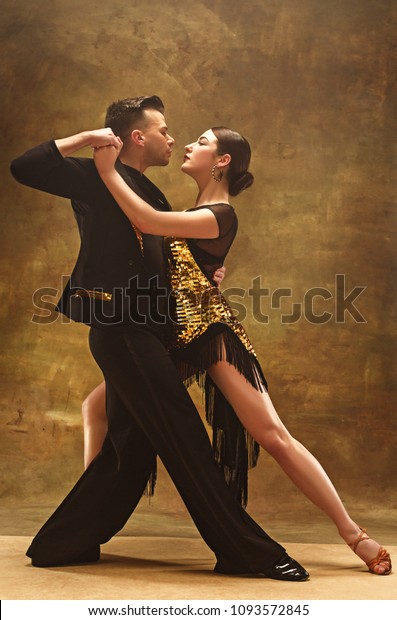 スタジオ背景に官能的なポーズで金ドレスを着た若いダンス社交場のカップル プロの踊り手がタンゴを踊る 社交ダンスのコンセプト 人間の感情 愛と情熱 の写真素材 今すぐ編集