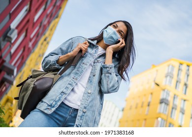 Young Dark Skinned Girl Student Wearing Medical Mask And Talking On Her Mobile Phone While Walking Outdoors.