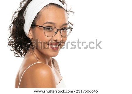Young dark skinned smiling woman with makeup, headband and glasses posing on a white studio background
