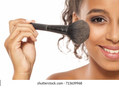 a young dark skinned woman applies a highlighter on her face