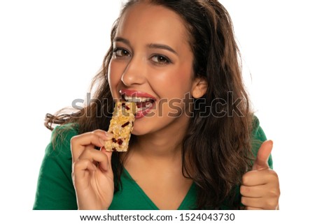 young dark skinned woman eating cereal bar on white background