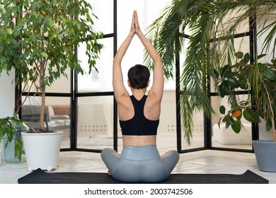 Young Darkhair Woman Practicing Yoga In The Morning At Her Home Near Plants. The Woman Is Engaged In Self-determination, Doing Yoga Exercises