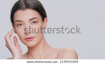 Young dark-haired beauty model posing for skin care products commercial, touches her face gently sliding hand from her cheek down to the chin on grey background | Skincare concept