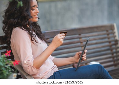 Young Dark-haired Curly Woman Pays For Purchases Online Through Internet Banking Using A Tablet. 35 Year Old Model Sits On The Street In The City Center.