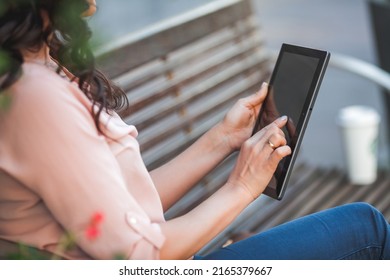 Young Dark-haired Curly Woman Pays For Purchases Online Through Internet Banking Using A Tablet. 35 Year Old Model Sits On The Street In The City Center.