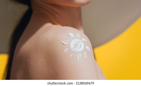 Young Dark-haired Woman In A Big White Hat And Yellow Swimsuit Applies Sunscreen On Her Shoulder Against Yellow Background | Sunscreen Application | Sun Shape