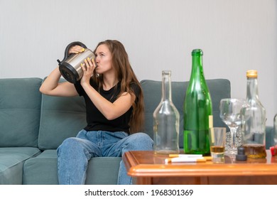 Young Dark-haired Woman Is Sitting On A Sofa With Her Eyes Open, Drinking Water From A Teapot After A Wild Party, With Empty Bottles Next To Her