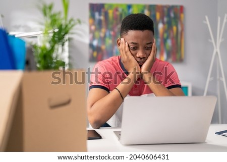 Young dark-skinned boy sits slumped in front of computer, props hands under face, bad news, losing money, overwork, sadness, fatigue, heartbreak, stress, disappointment