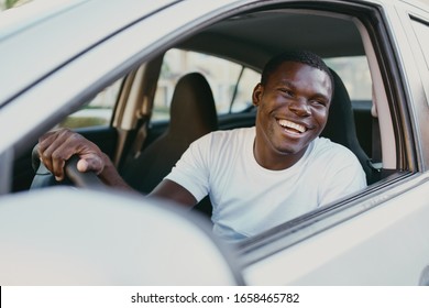 a young dark-skinned man sitting in a car in a white T-shirt