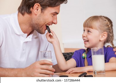 Young daughter is feeding her father with chocolate cookies
