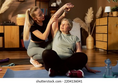 Young Daughter Helping Elderly Mother Doing Exercises Stretching Together. Women Having Fun On Yoga Mat In Lotos Pose Breathing Maditating.