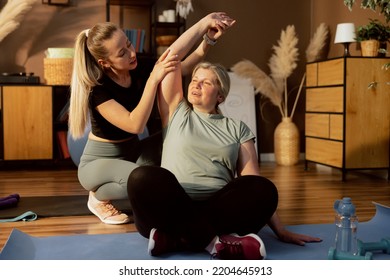 Young Daughter Helping Elderly Mother Doing Exercises Stretching Together. Women Having Fun On Yoga Mat In Lotos Pose Breathing Maditating.