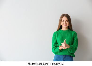 Young deaf mute woman using sign language on light background