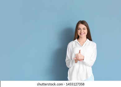 Young deaf mute woman using sign language on color background