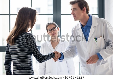 Young dedicated reliable physician and female patient shaking hands before consultation in the office of a modern medical center