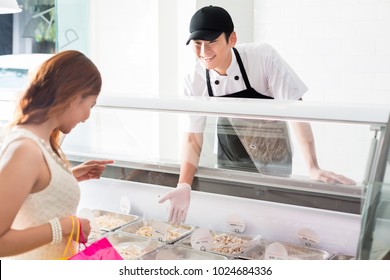 Young deli assistant serving a customer pointing to a selection of food in a glass counter as she tries to make a decision - Powered by Shutterstock