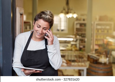 A Young Deli Employee Talking On The Phone While Working On A Tablet