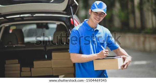 Young delivery\
man checking the products to customer while standing right next to\
his car and smiling to the camera\
