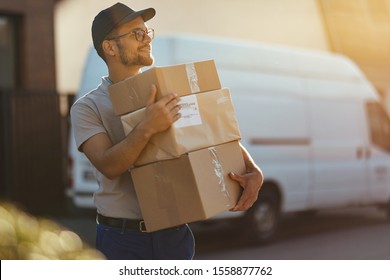 Young delivery man holding stack of packages while making home delivery at residential district. 
