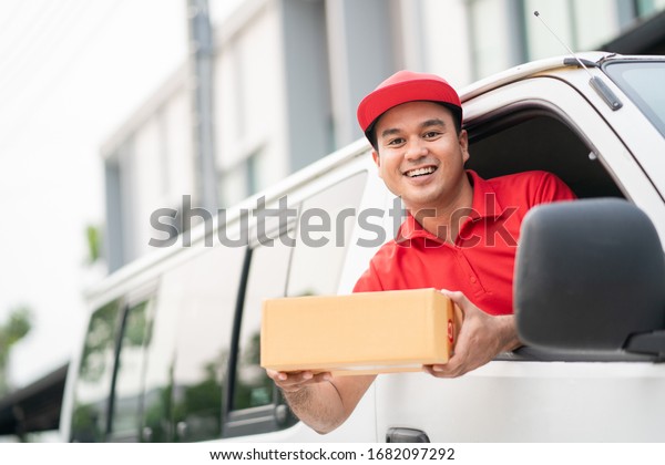 Young delivery man\
in red uniform driving van,truck to sending parcel cardboard box\
cargo service concept.