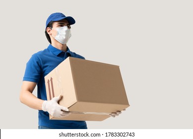 Young delivery man wearing face mask and gloves while carrying cardboard box during coronavirus outbreak