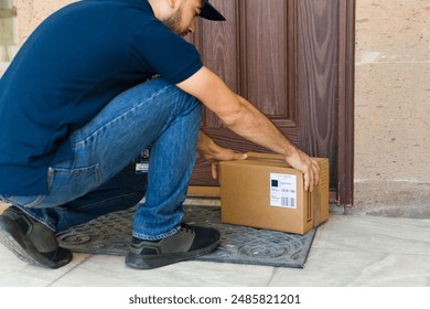 Young delivery man wearing a uniform and leaving a box at the entrance of a house - Powered by Shutterstock