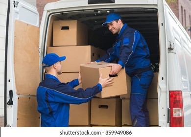 Young delivery men unloading cardboard boxes from truck
